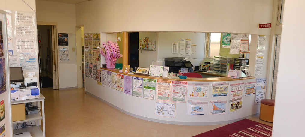 Clinic reception desk with informational posters and decorations, including flowers and a teddy bear, highlighting key messages for visitors.