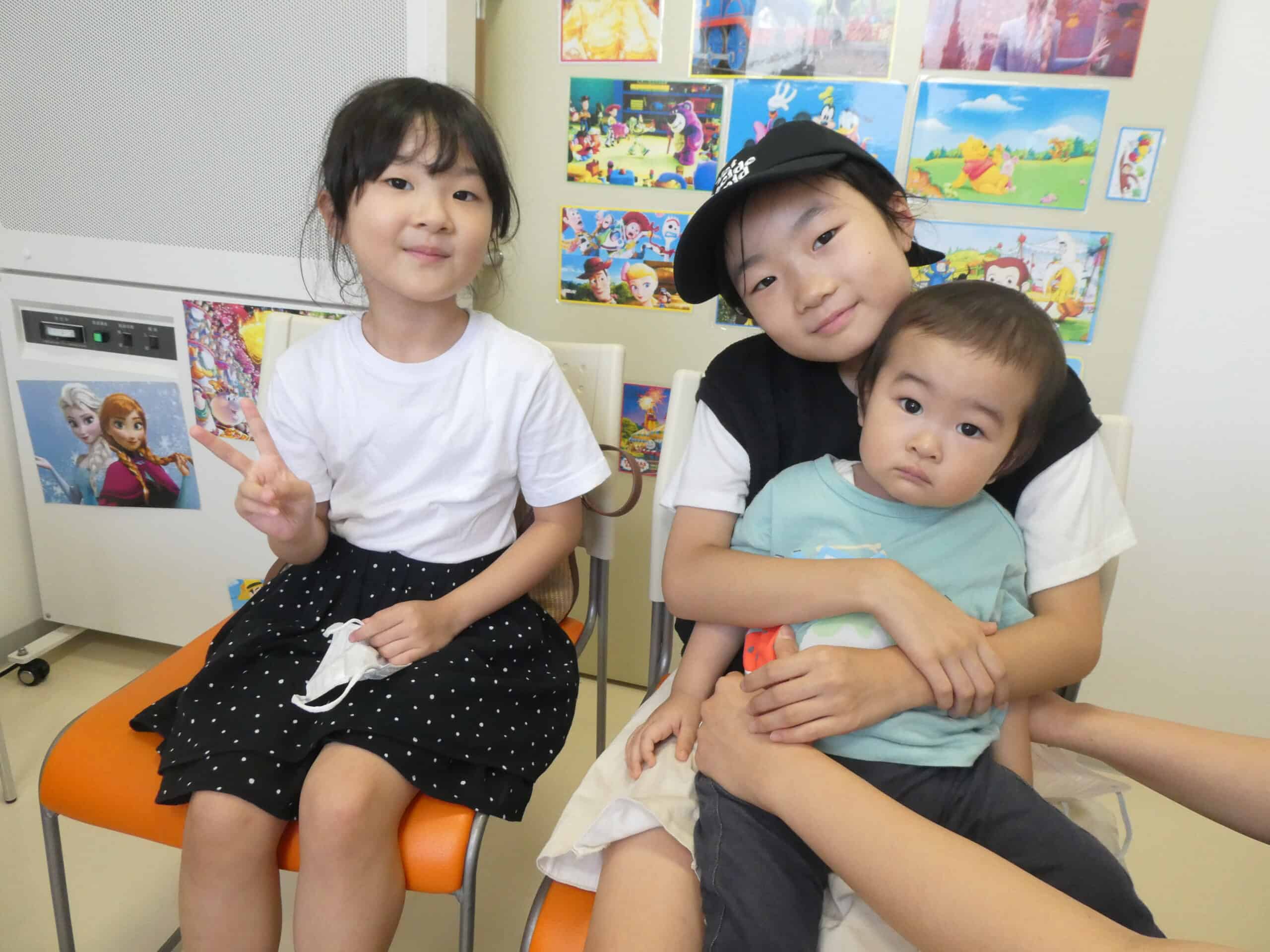 明るい待合室で、小児科医院の子供たちが笑顔でリラックスした時間を過ごしています。子供たちの健康と笑顔をサポートする石田小児科医院の温かい雰囲気を伝えています。.